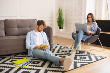 Sınavdan önce çalışan gülümseyen genç adam, karısı dizüstü bilgisayarla çalışıyor.