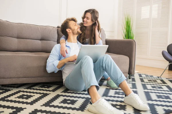 Young couple in denim sitting on a floor watching something and looking romantic — Stock Photo, Image