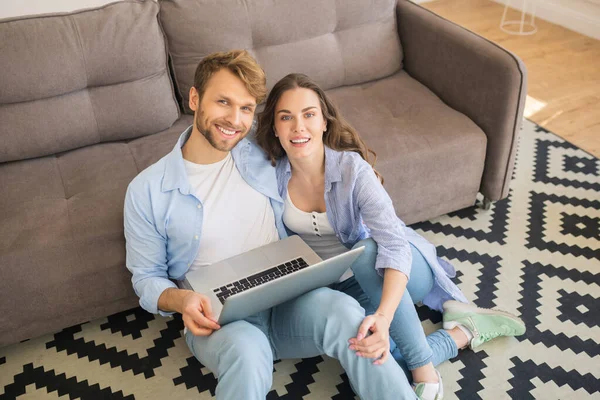 Joven feliz pareja en denim sentado en un suelo viendo algo y sonriendo — Foto de Stock