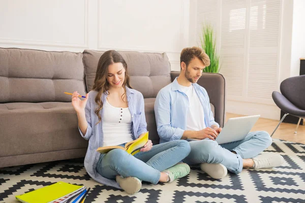 Pareja joven sentada en el suelo estudiando juntos y buscando involucrados — Foto de Stock