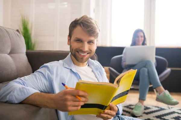 Sonriente joven estudiando antes del examen, su esposa sentada detrás de él —  Fotos de Stock