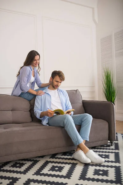 Young man studying before exam, his wife touching his shoulder — Stock Photo, Image