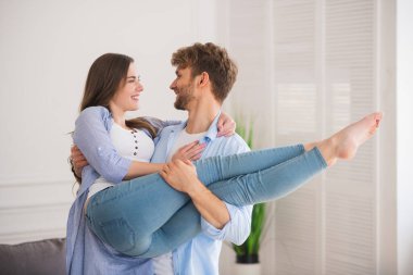 Genç adam karısını kucaklıyor ve mutlu bir şekilde gülümsüyor.