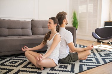 Nilüfer çiçekli beyaz tişörtlü genç çift sırt sırta poz veriyor ve huzurlu görünüyorlar.