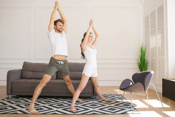 Pareja joven en camisetas blancas haciendo yoga en casa —  Fotos de Stock