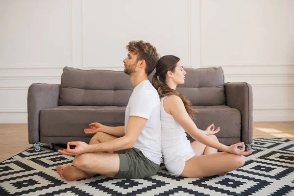 Young couple in white tshirts sitting in lotus pose back to back with eyes closed — Stock Photo, Image