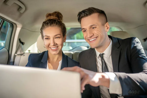 Obchodní muž a žena s notebookem na zadním sedadle v autě — Stock fotografie