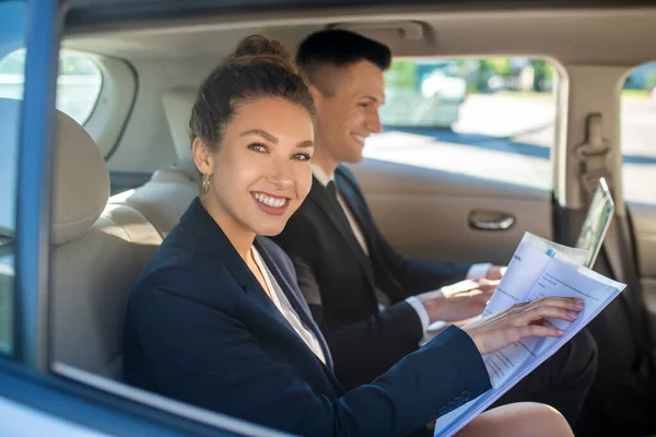 Mosolygós nő papírokkal férfi laptoppal az autóban — Stock Fotó