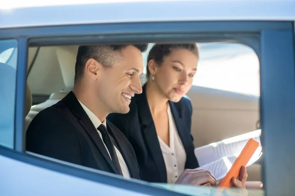 Homem atraente com tablet e mulher atenciosa com documentos no carro — Fotografia de Stock