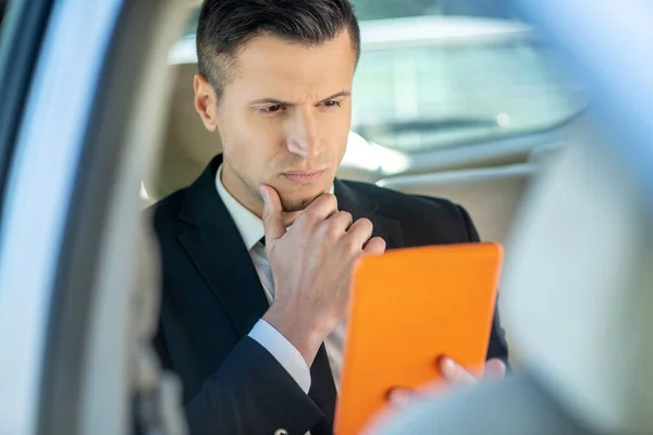 Successful man carefully looking at the tablet in the car. — Stock Photo, Image