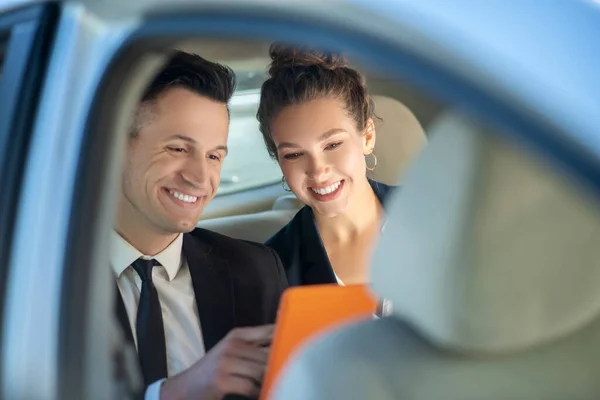 Exitoso hombre y mujer alegre mirando la tableta en el coche . — Foto de Stock