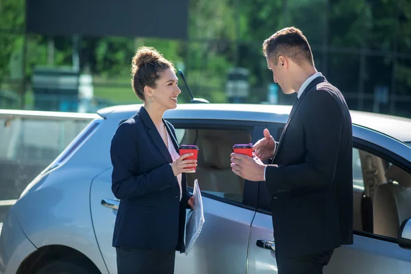 Homem sério e mulher sorridente com copos de café perto do carro — Fotografia de Stock