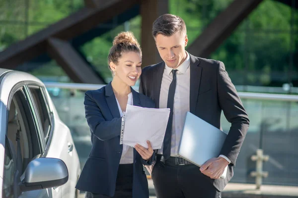 Mujer con papeles y hombre con portátil cerca del coche — Foto de Stock