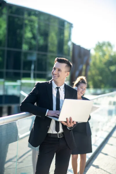 Vrolijke zakenman met laptop op zoek naar kant, vrouw op afstand — Stockfoto