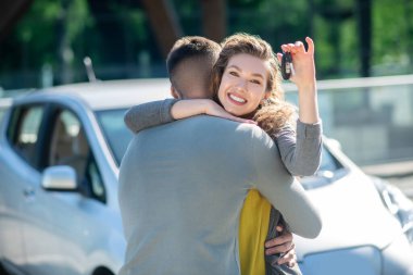 Minnettar, neşeli, anahtarı olan bir kız bir adama sarılıyor.
