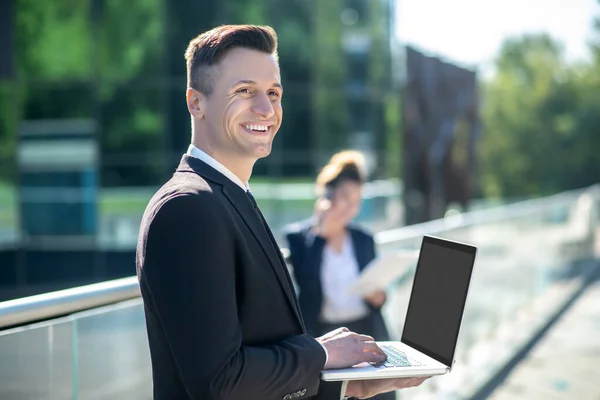 Homem usando laptop com sorriso de dentes brancos em pé na rua — Fotografia de Stock