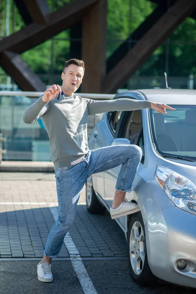 Молодий дорослий чоловік стоїть біля машини, показуючи ключі — стокове фото