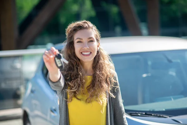 Mulher sorridente com chave de carro na mão estendida — Fotografia de Stock