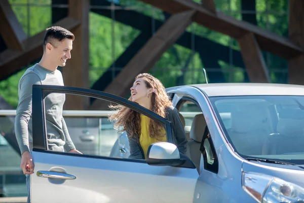 Jovem mulher bonita abrindo a porta do carro e falando com o jovem — Fotografia de Stock