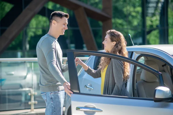Молода красива жінка розмовляє з високим чоловіком, що стоїть біля машини — стокове фото