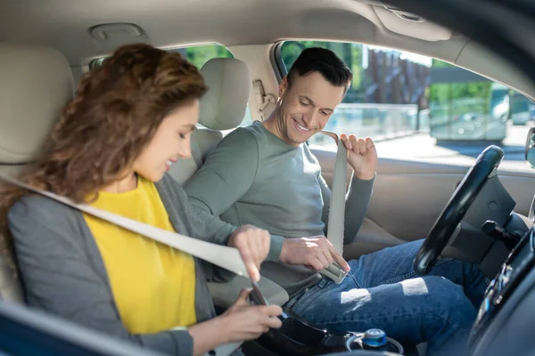 Mladý pár sedí v autě, žena opravuje bezpečnostní pás — Stock fotografie