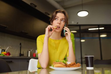 Akıllı telefondan konuşan bir kadın patates kızartması yiyor..