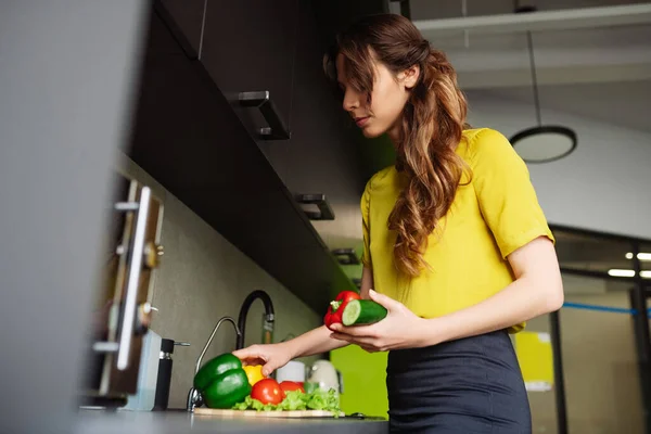 Donna soddisfatta in piedi in cucina raccogliendo verdure — Foto Stock