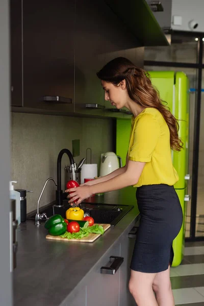 Jonge vrouw in gele blouse en rok wassen pepers — Stockfoto