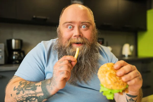 Primer plano del entusiasta hombre de ojos azules con hamburguesa y papas fritas —  Fotos de Stock