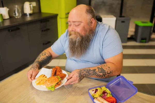 Hombre gordo feliz con tatuajes tomando plato con hamburguesa —  Fotos de Stock