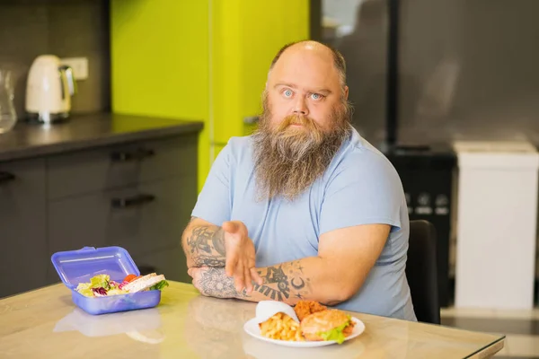 Hombre barbudo sentado en la cocina a la mesa con comida —  Fotos de Stock