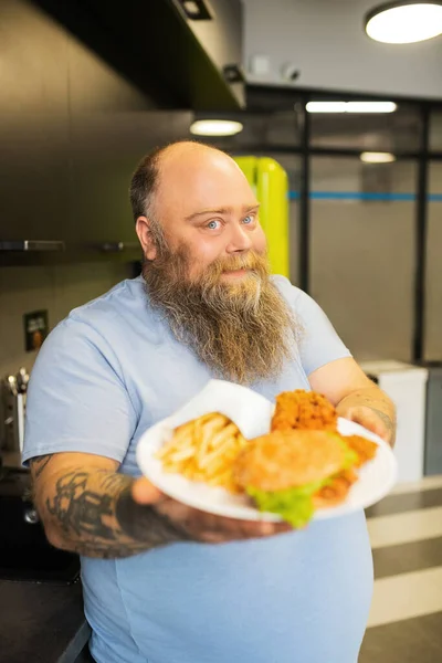 Homme barbu souriant tenant une assiette de nourriture vers l'avant — Photo