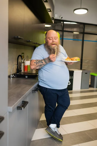 Übergewichtiger Mann isst Pommes in der Küche — Stockfoto