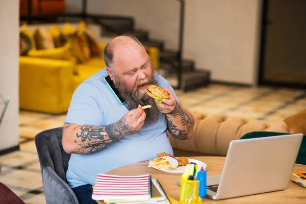 Homem gordo careca abrindo a boca para morder um pedaço de hambúrguer — Fotografia de Stock