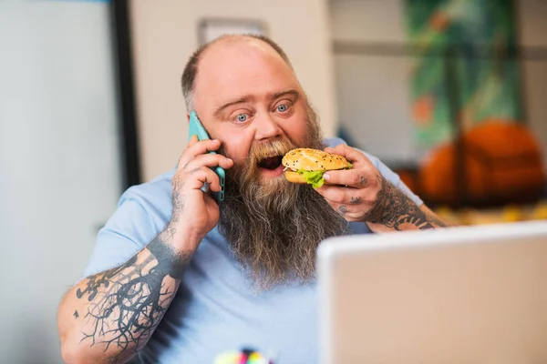 Mann mit Glatze telefoniert und isst einen Burger — Stockfoto