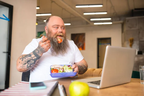 Bald bearded man in white tshirt having lunch sitting at the table — Stock Photo, Image