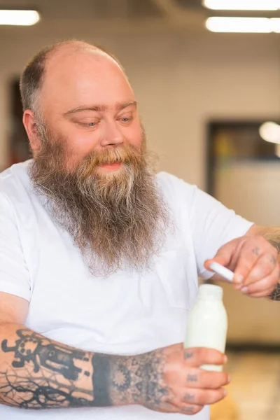 Łysy brodaty pulchny człowiek otwierając butelkę z mlekiem — Zdjęcie stockowe