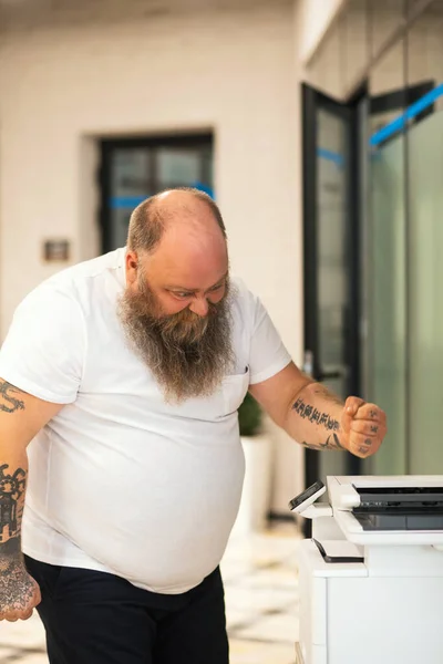 Bald bearded plus size man making copy on xerox and feeling angry