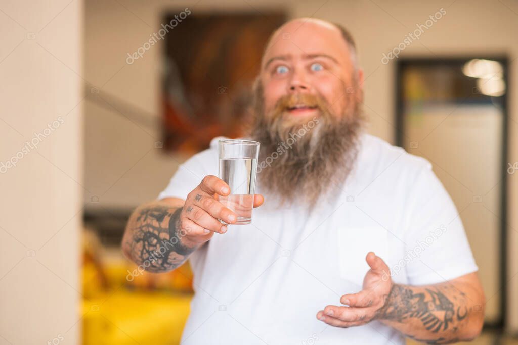 Bald bearded plump man holding a glass of water in his hand