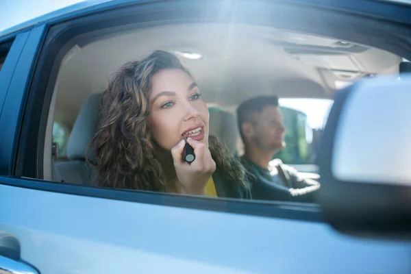 Beautiful woman painting lips in car looking in side mirror — Stock Photo, Image