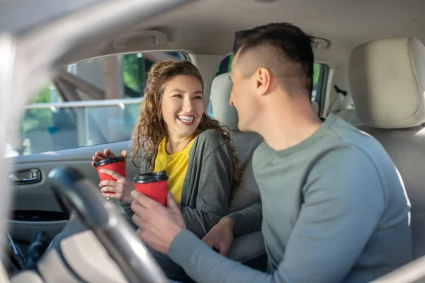 Mulher e homem sentados no carro com copos de café . — Fotografia de Stock