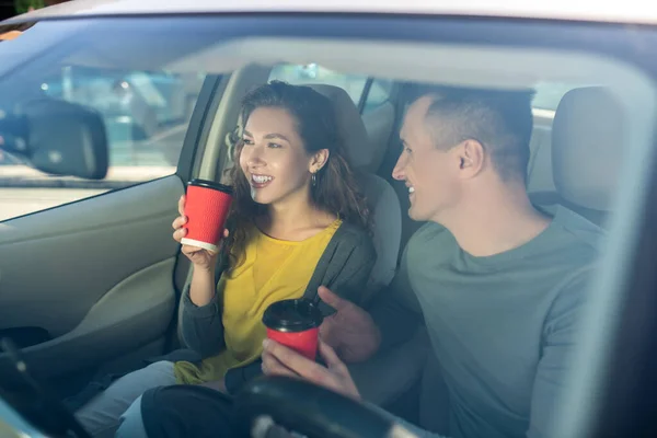 Mladý muž a žena pití kávy v autě — Stock fotografie