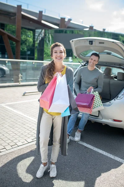 Mulher elegante alegre com compras e homem perto do carro — Fotografia de Stock