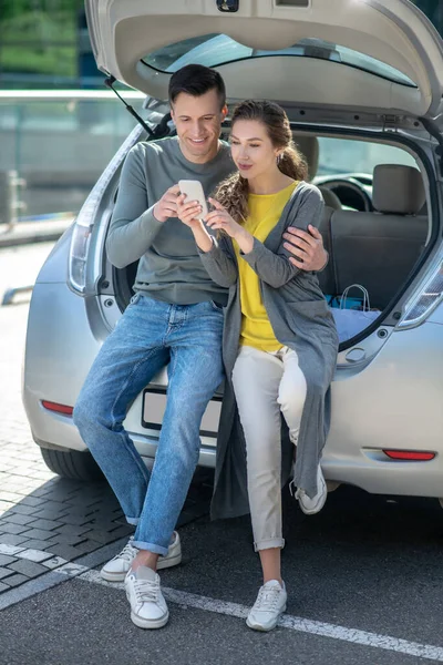 Молодий чоловік і жінка зі смартфоном відпочивають біля машини — стокове фото