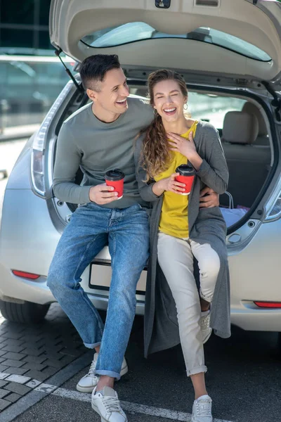 Jovem homem bonito e mulher bebendo café perto de um carro — Fotografia de Stock