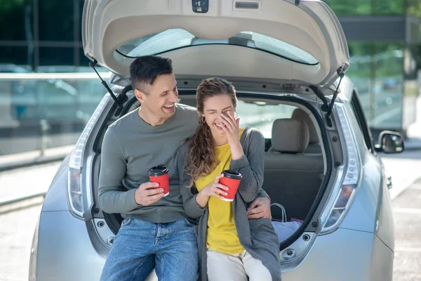 Сміється чоловік і жінка з кавою біля машини — стокове фото
