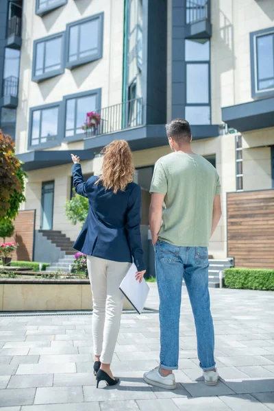 Elegante empresaria de pie en la calle y mostrando la casa a su cliente — Foto de Stock