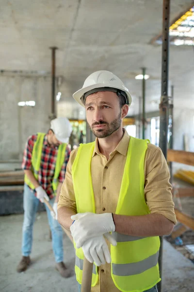 全身心投入工作的建筑工人身穿黄色背心，戴着手套休息，靠着手柄，同事们向他打招呼 — 图库照片