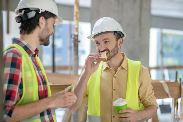 建筑工人穿着黄色背心和手套，喝咖啡，说话，微笑，吃饭 — 图库照片