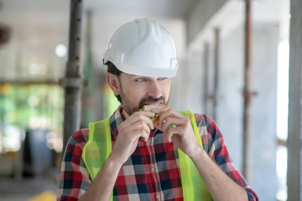 身穿黄色背心头戴安全帽的建筑工人咬三明治 — 图库照片
